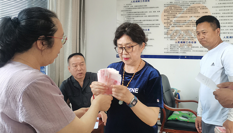 頭題片，5月30日，某藥業(yè)公司按協(xié)議約定完成第一期履行義務(wù)，將十萬現(xiàn)金交到法院，調(diào)解員付菊（左一）清點(diǎn)無誤之后交到農(nóng)民工委托代理人徐某手中