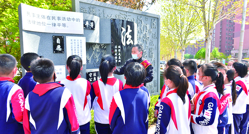 頭題圖，普法志愿者在憲法墻前給學(xué)生們普及法律知識(shí)。